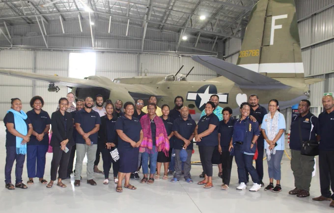 Group photo of participants and course staff posing in front of a vintage military aircraft inside a spacious hangar at the PNG Museum. 