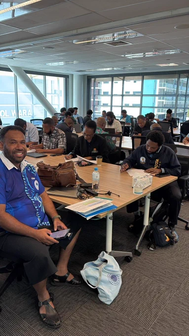 Photo of participants seated at tables in a modern office space, engaged in writing and using laptops during a workshop.