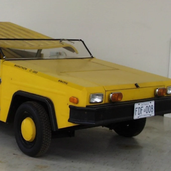 Compact yellow vintage car with a flat hood and black bumper, parked indoors on a smooth floor.