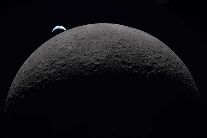 A close-up view of the Moon's cratered surface against black, with a small blue crescent of Earth rising above the lunar horizon.