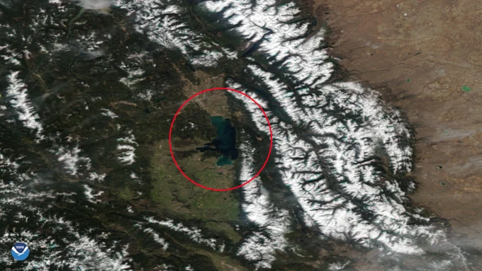 A satellite image shows a blue lake (within a red circle) next to snow-covered mountains.