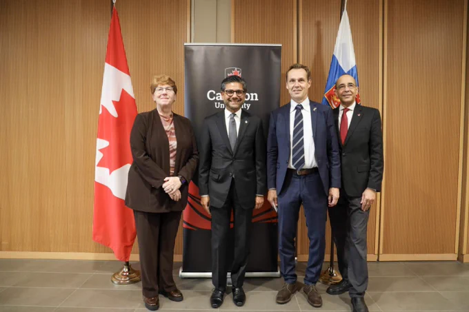 Four people in business attire posing in front of a Carleton banner and the Canadian and Finnish flags.