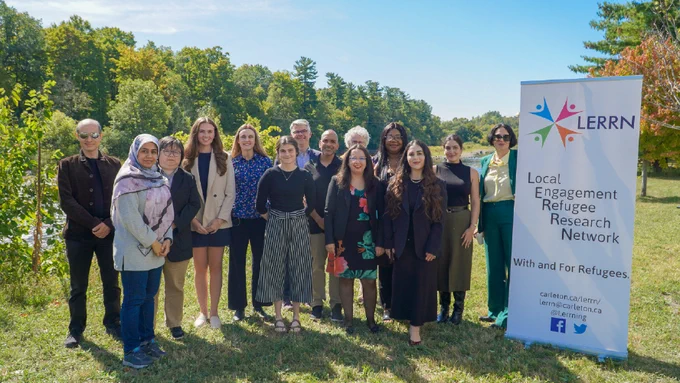 A group shot of 14 people standing next to a LERRN banner, surrounded by lots of greenery.