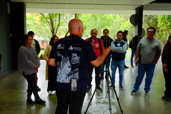 A backshot of a man in a t-shirt next to a tripod in front of a small group of people.