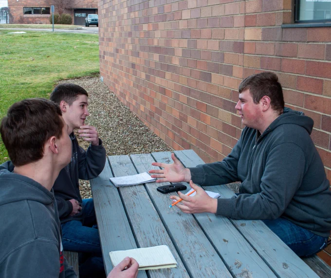 3 current livestock judging team members learning from one another outside at a picnic table on campus. 