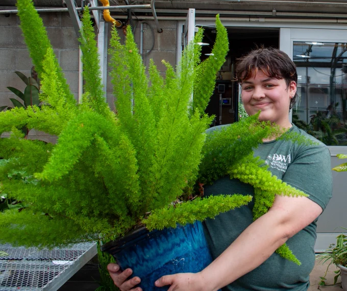 Student in the greenhouse holding a plant and posing for a picture. 