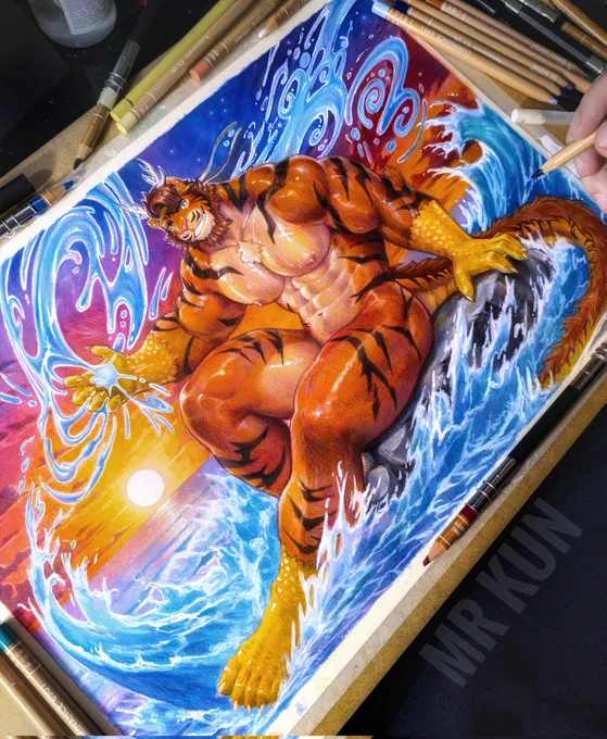 An angled photo of a traditional handmade illustration in progress, showing a muscular anthropomorphic tiger man as he sits on a rock at the sea while casting water magic around jim. The background is a sunset and the sea. Various art supplies, mainly color pencils lay around the painting. 