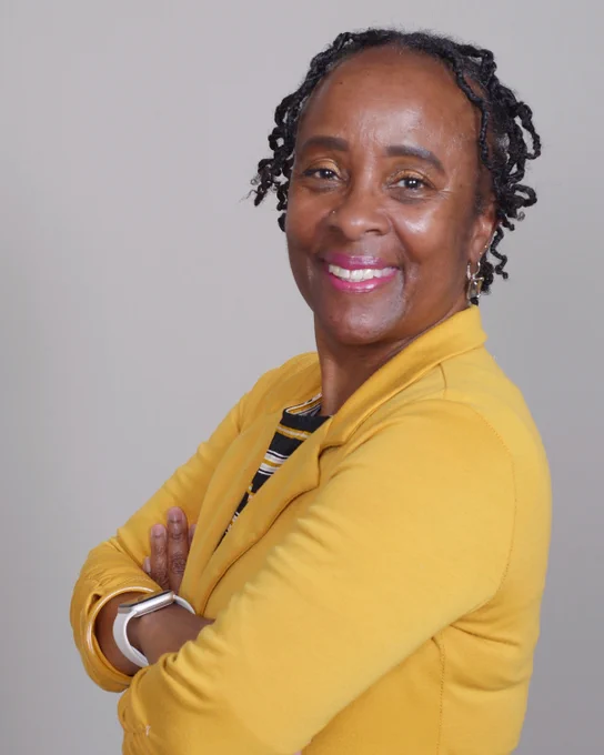 Professional headshot portrait of Cindy Canty-Dumas, MSW. Canty-Dumas is standing sideways with crossed arms, smiling, and is wearing a yellow suit jacket.