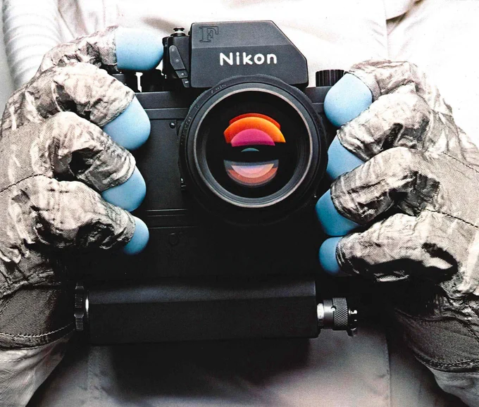 A close-up image of a Nikon camera being held by gloved hands.