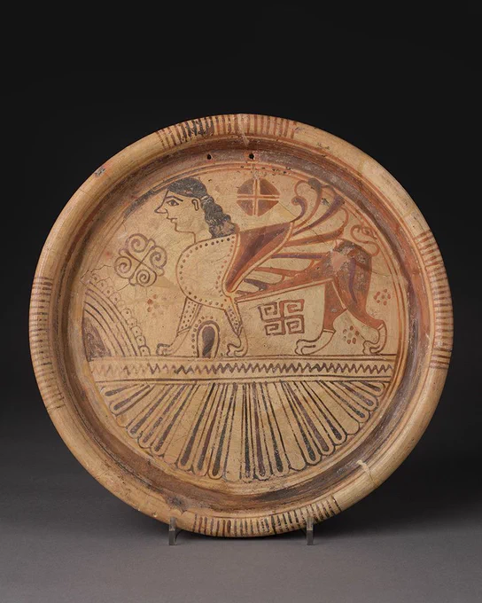 A plate decorated with the an image of a sphinx with a lion’s body, a bird’s wings and a woman’s head. 
