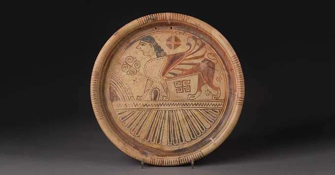 A plate decorated with the an image of a sphinx with a lion’s body, a bird’s wings and a woman’s head. 