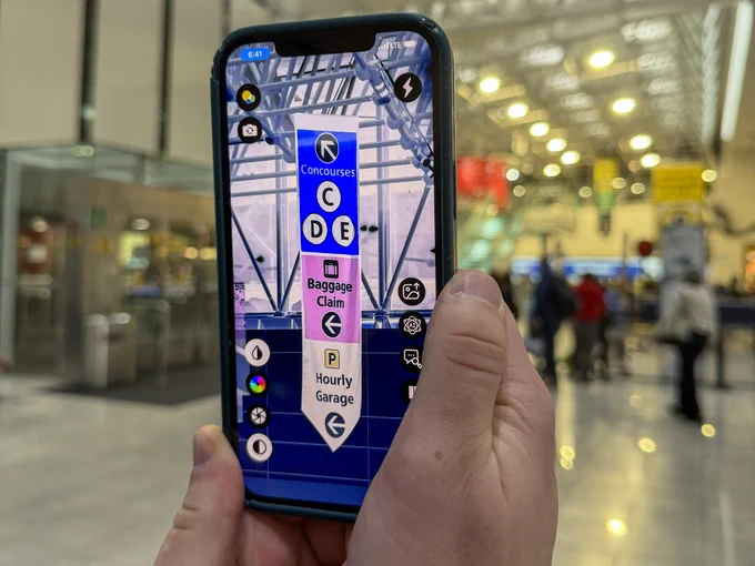A cell phone with an assistive app displays a navigational banner hanging inside BWI Thurgood Marshall Airport.