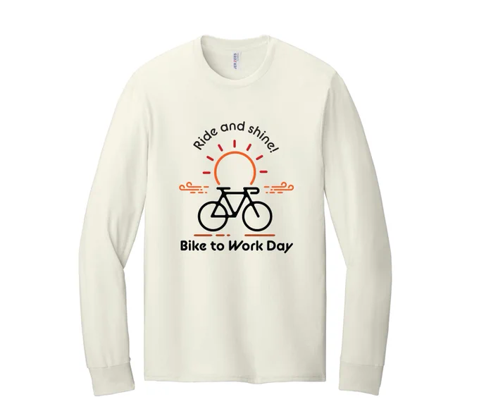 A long-sleeve shirt featuring a graphic of a bicycle with a rising sun behind it. The design includes the text "Ride and shine! Bike to Work Day". The shirt is a light beige color.