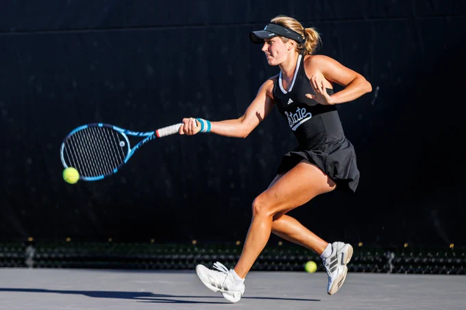 A women’s tennis player sprints across the court and reaches out to return a forehand, eyes locked on the ball during a match.
