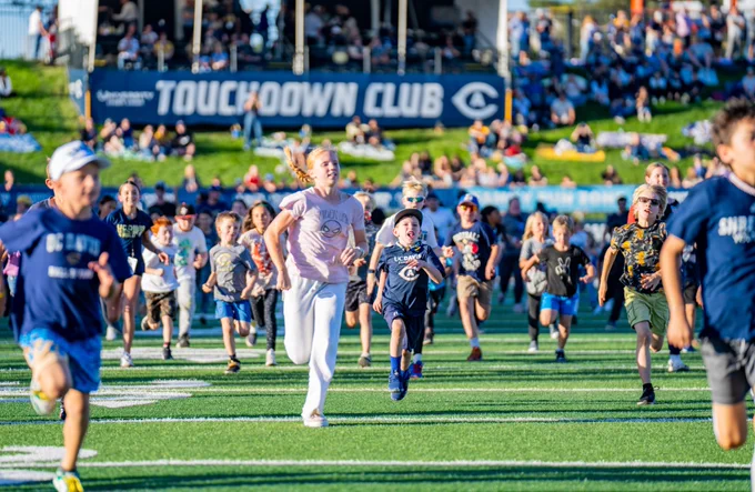 Image Description:
1. Photo of kids running out during a kids run before a UC Davis football game
2. Photo of young kid on shoulders of an adult man
3. Informative graphic with spring game information listed on a blue graphic and a photo of a student athlete giving a high five to a kid
4. Photo of a UC Davis football student athlete giving a high five to a young kid during walk into stadium