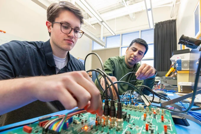 Two people check wires and connectors on a circuit board. 