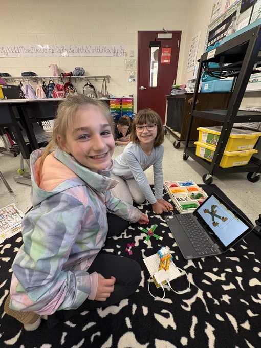 2 students  smiling while building a Spike Lego ferris wheel.