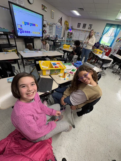 Two girls smiling as they build a Spike Lego ferris wheel.