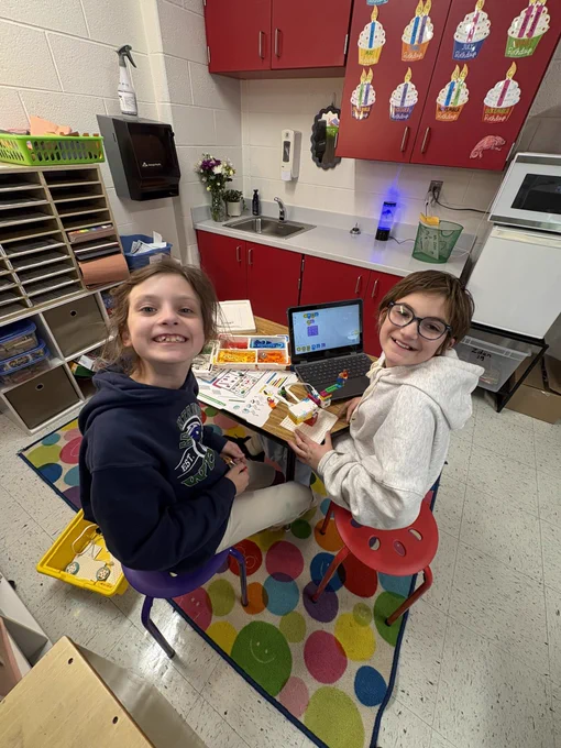 Two girls smiling as they work on building a Spike Lego twirling tea cup ride.