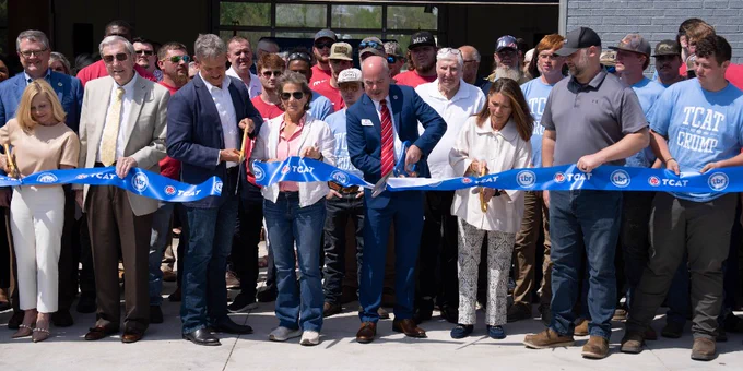 A group of individuals cut a ribbon outside a new building. The ribbon features the Tennessee College of Applied Technology logo. 