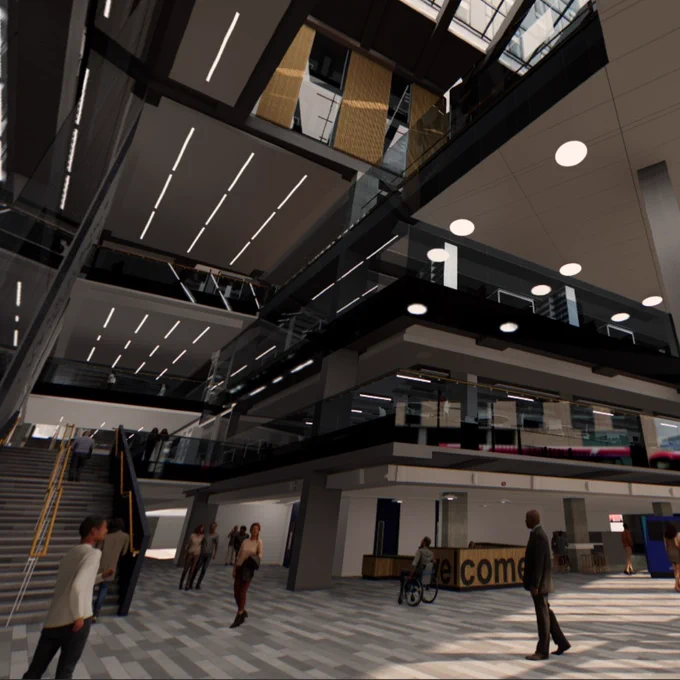 Spacious modern reception with high ceilings, glass railings and people walking near a welcome desk under natural light.