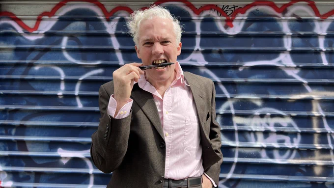 Poet Jason Stoneking clenches his pen between his teeth in a promo shot for his featured performance at Spoken Word Paris