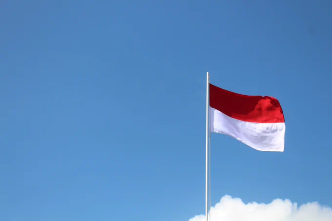 The flag of Indonesia flying in the wind against a blue sky background.