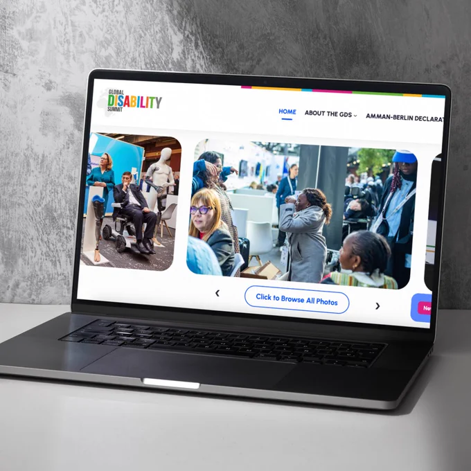 A laptop displaying the Global Disability Summit (GDS) website homepage, showing images from the event and a navigation menu at the top.