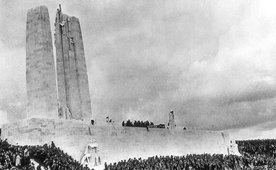Crowd gathered at the Vimy Memorial in France during an unveiling ceremony, with the tall stone monument rising above a large assembly of people on the surrounding steps and grounds.