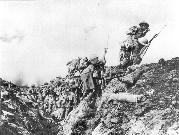 Canadian soldiers advancing up the side of a trench with rifles and equipment, climbing steep earthworks during combat operations at Vimy Ridge.