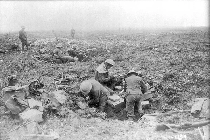Canadian soldiers operating and supplying a machine gun position in a shell-pocked landscape at Vimy Ridge, with other troops visible in the distance.