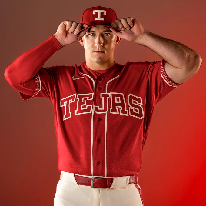 Wyatt Langford posing for a photo in the new Rangers City Connect uniform. He’s grabbing the brim of his hat with both hands.