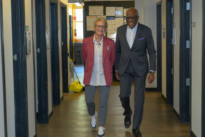 President Cantwell and UW President Jones walk in a hallway lined with doors smiling at the camera 