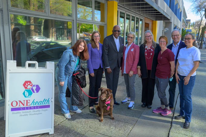 A One Health Clinic sign on the left with a group of people, including President Cantwell and UW President Jones stand for a photo