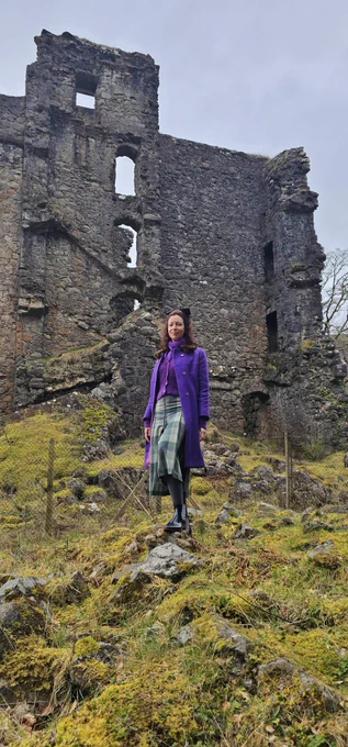 Me posing with a castle ruin in the background on the way to the Isle of Skye. The grass and moss is bright green while the castle is an ominous grey.