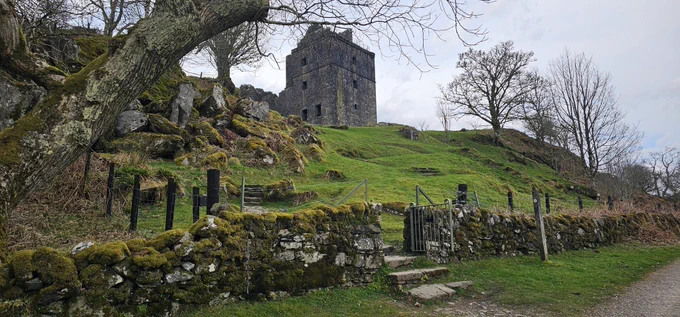 Another castle ruin sitting on top of a bright green hill, surrounded by a stone fence.