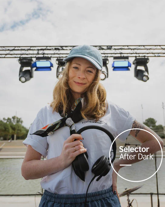 A smiling Tina Edwards wearing a light blue cap holds headphones, in front of an outdoor stage setup by water. “Selector After Dark” is in white text in a transparent circle in the bottom right.