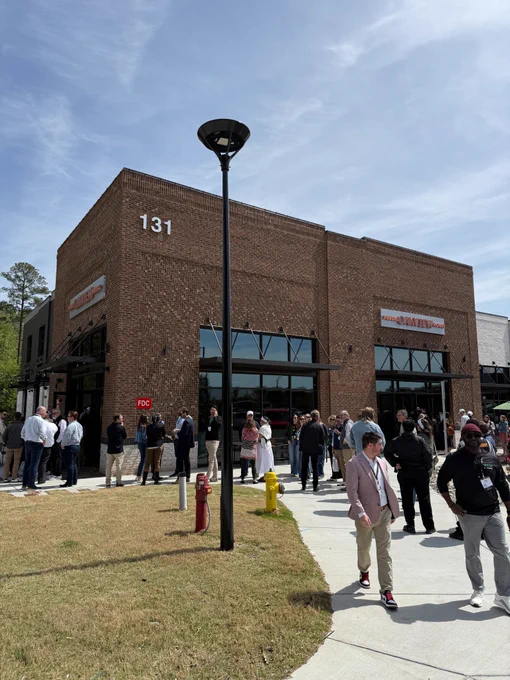 Outside of a brick building with a grassy space and people standing together talking.
