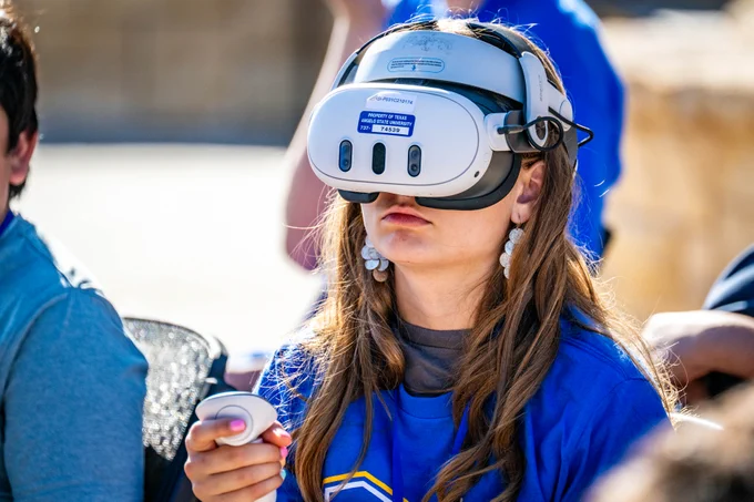 A person wearing a blue shirt and holding a handheld controller is using a virtual reality headset. 