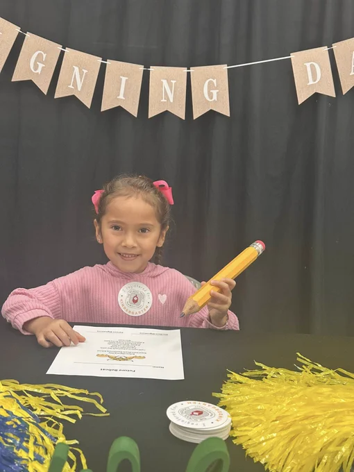 Young girl holding a large pencil at a table