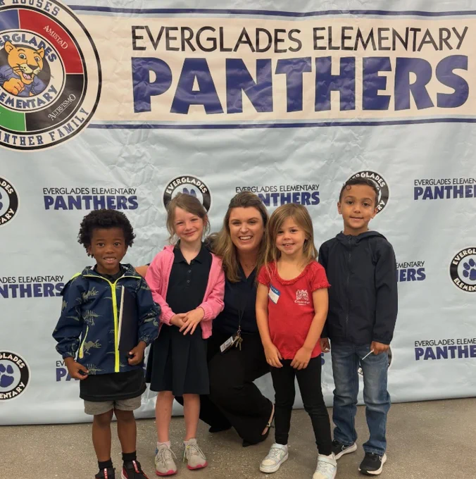 Four young students standing with a principal in front of a sign for Everglades Elementary School.