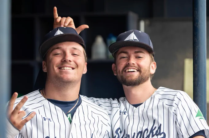 Two baseball team members smile for the camera from the dugout