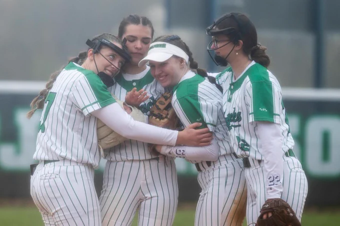 Four softball players hug each other