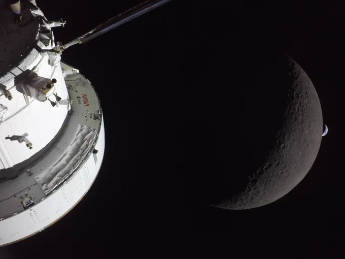 Close-up of a spacecraft module orbiting near a crescent moon with Earth faintly visible in the background.