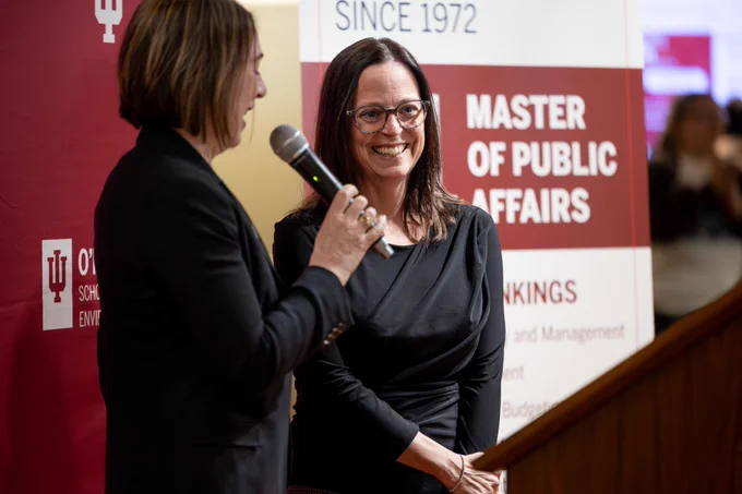 Jill Nicholson-Crotty smiles while Dean Sian Mooney holds a microphone, speaking at the O'Neill rankings celebration event. A sign in the background reads "#1 Master of Public Affairs".