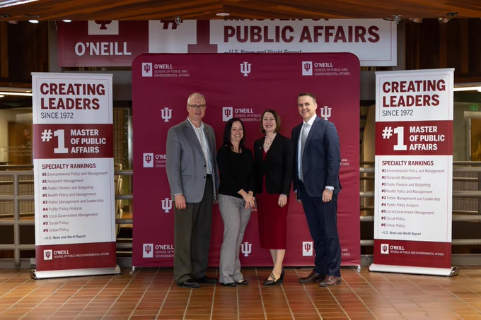 Four O'Neill Dean's are standing in front of a backdrop that reads "O'Neill School of Public and Environmental Affairs" and "Creating Leaders Since 1972" at Indiana University. Two banners highlight that the university's Master of Public Affairs program is ranked #1.