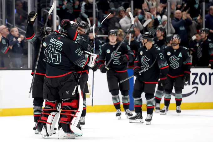 a photo of the Seattle Kraken skating to hug goaltender Joey Daccord following the win.