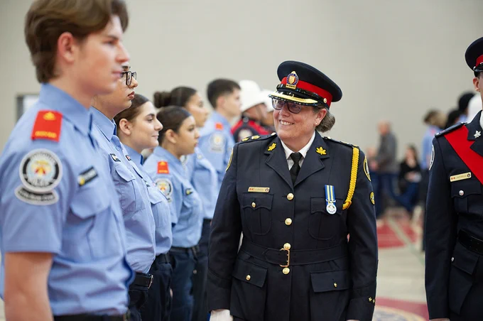 A person wearing a police uniform walks past a row of young people standing at attention.
