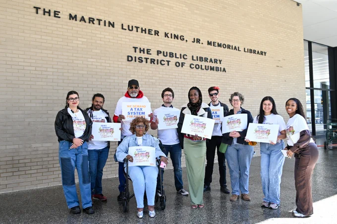 A group of people gathered together outside the MLK library in DC, holding signs that read "We demand a tax system for justice" and "Taxes support thriving communities." 