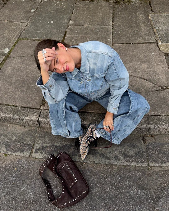 An image of a person wearing a pair of leopard print Vans Super Lowpro trainers with a denim outfit whilst sitting on a pavement. 